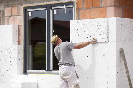 Ouvrier en bâtiment installant un panneau d'isolation thermique extérieure sur façade de maison en construction