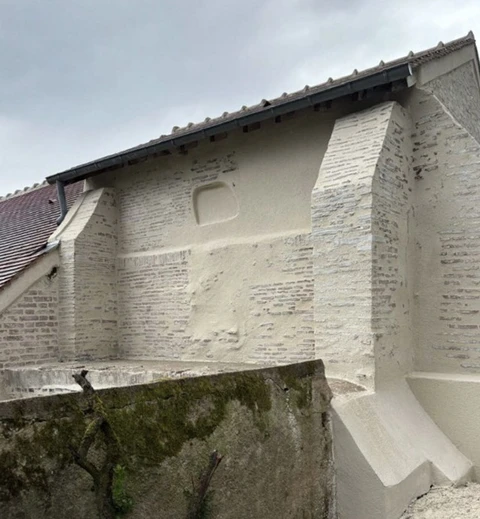 Façade de bâtiment en cours de rénovation avec mur en briques apparentes partiellement recouvert d'enduit blanc écaillé