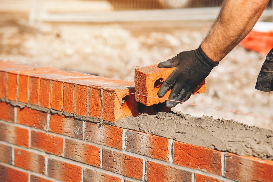 Deux ouvriers équipés de casques de sécurité blancs nettoient la façade vitrée d'un immeuble moderne en hauteur